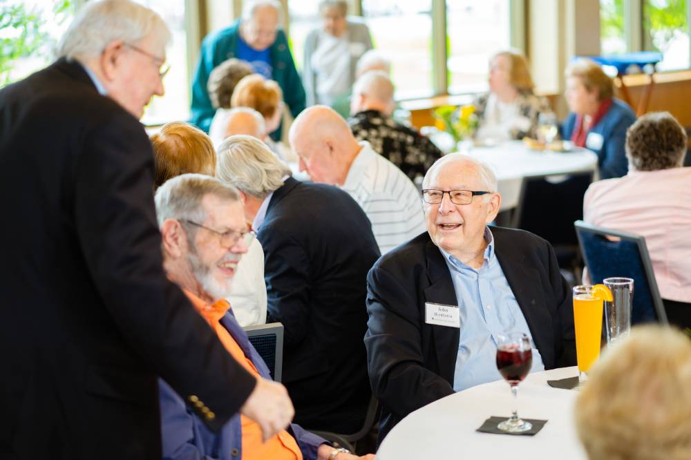 President Emeritus Don Lubbers talking to guests seated at a table at the Retiree Reception.